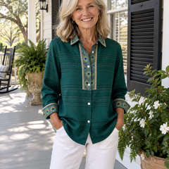 Woman wearing the Sofia emerald green peacock feather blouse with white trousers