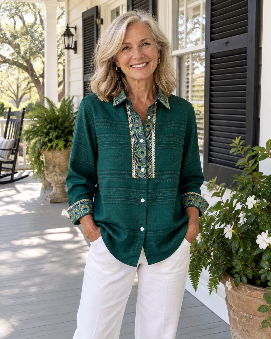 Woman wearing the Sofia emerald green peacock feather blouse with white trousers